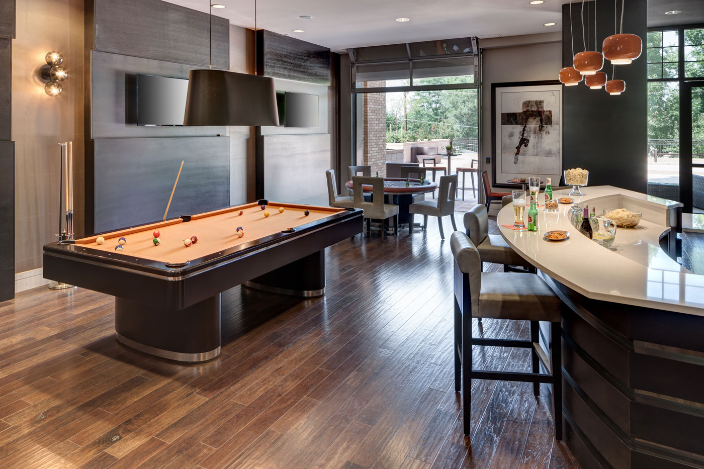 Hardwood floors, wood finishes, pool table, and modern rounded bar in clubhouse of luxury multifamily space in Colorado.
