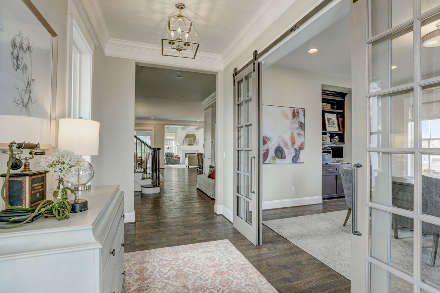 Foyer with sliding grey barn doors into home office and a view of open living area in Colorado model home.