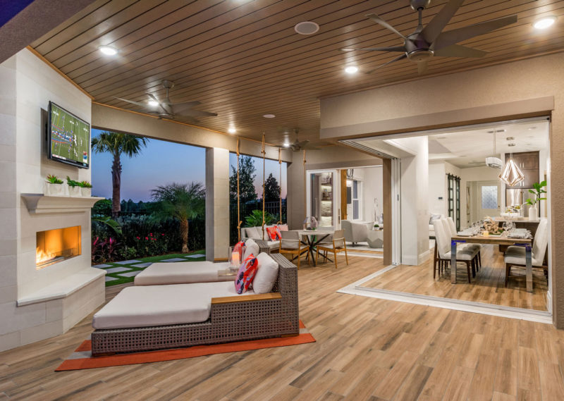 Award winning outdoor living space with lounge chairs, fireplace and open doors into home dining and living room in Florida.