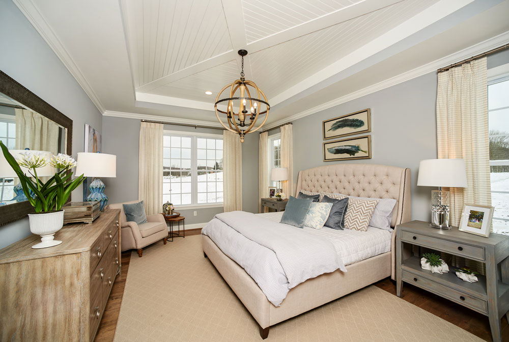 Sophisticated farmhouse master bedroom with tan furnishing, light blue walls and a white wood plank ceiling in Pennsylvania
